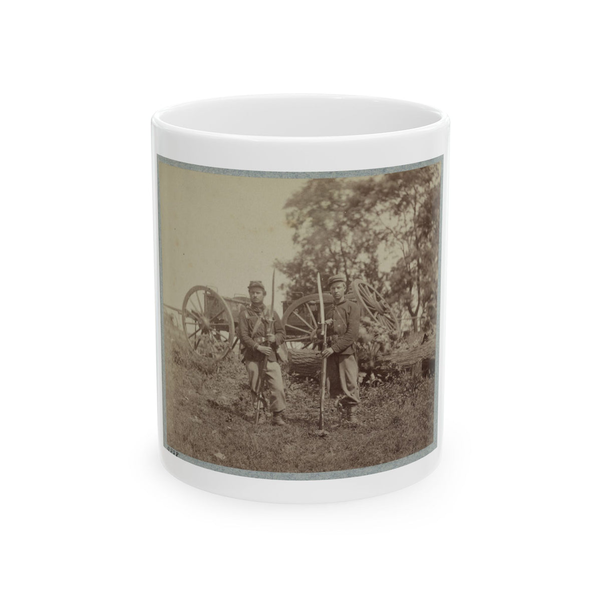 Sepia-toned print of two soldiers with bayoneted rifles standing in a field before wagon wheels and a fallen log.