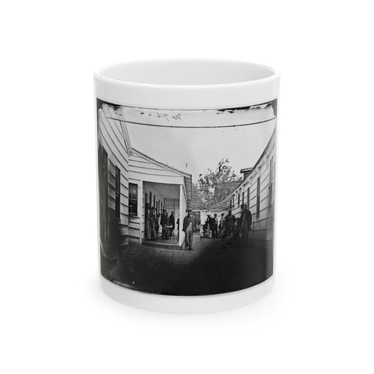Monochrome 1860s scene of men on a wooden plank walkway between clapboard buildings, one leaning on a crutch.