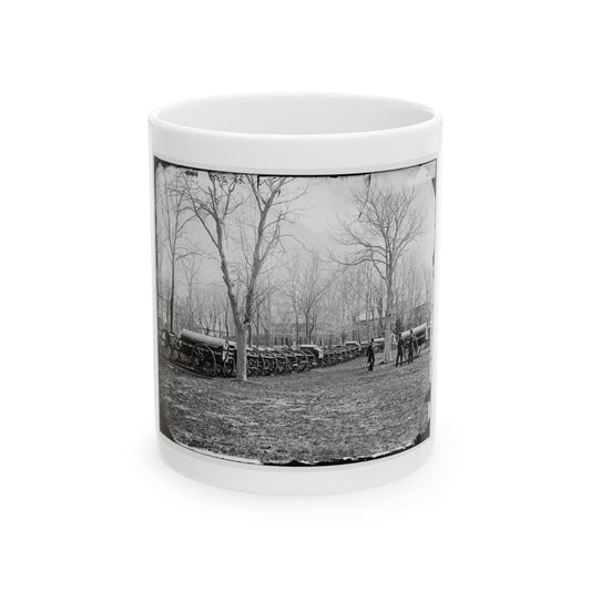 Black and white historical view of covered army wagons lined up on a field beneath bare trees, with two men nearby.
