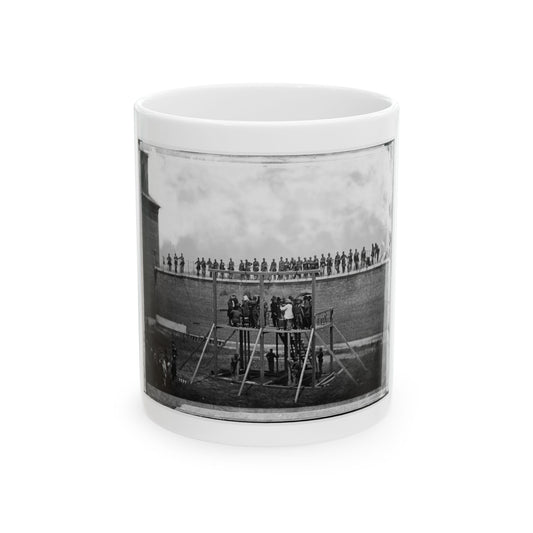 Black and white 1860s view of a gallows before a tall brick wall lined with soldiers and onlookers.