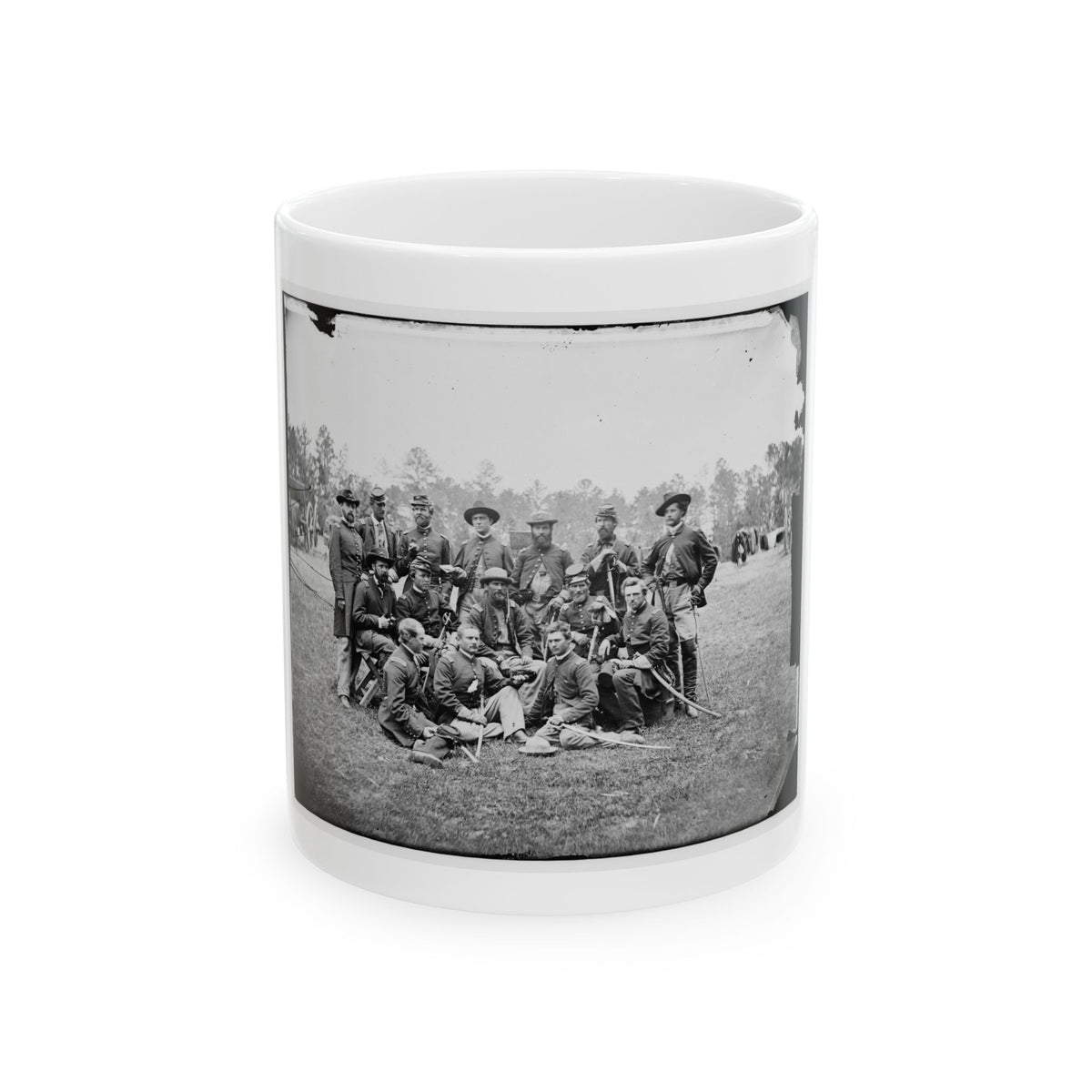 Black and white group portrait of about fourteen uniformed men with sabers posed on a grassy field before trees.