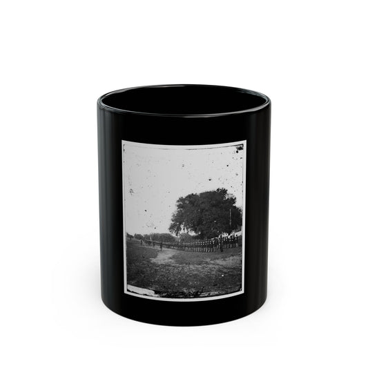 Black-and-white 1860s view of a long line of uniformed soldiers across a field beside an oak tree.