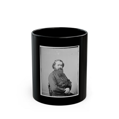 Black and white studio portrait of a bearded man in a dark military coat seated on a wooden chair.