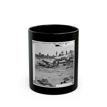 Black-and-white view of soldiers around a dismounted cannon amid sandbags, cannonballs and scattered debris.