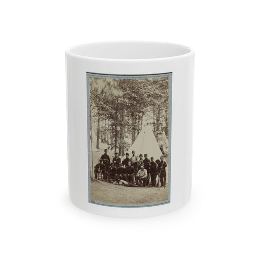 Sepia print showing about fifteen soldiers posed before a white conical tent beneath tall pine trees.