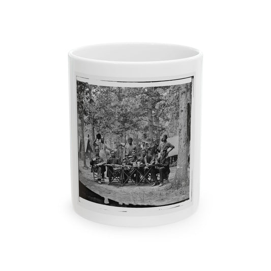 Black and white print of uniformed men seated at a camp table under trees, with attendants standing behind.