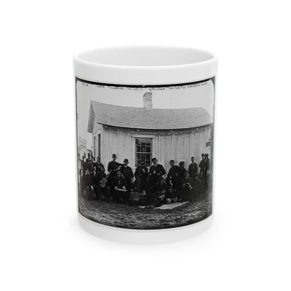 Black-and-white 19th-century print of about twenty uniformed soldiers with a guitar in front of a wooden barracks.