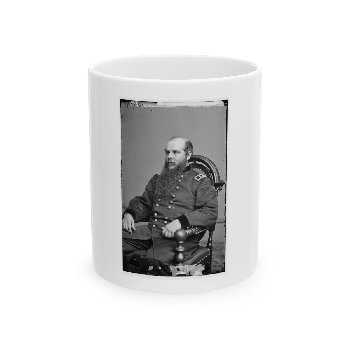 Black and white vintage portrait of a long-bearded man in a military coat seated in a carved wooden armchair.