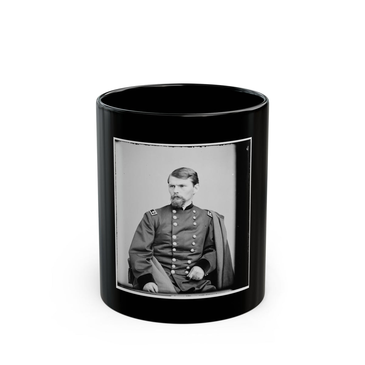 Black and white vintage studio portrait of a seated bearded man in a double-breasted coat, with a draped cape.
