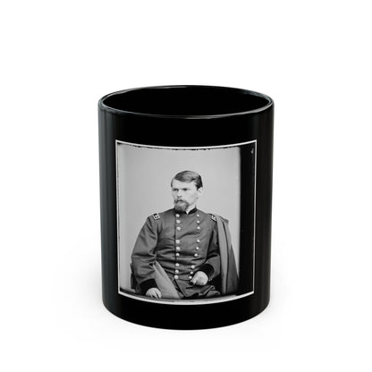 Black and white vintage studio portrait of a seated bearded man in a double-breasted coat, with a draped cape.