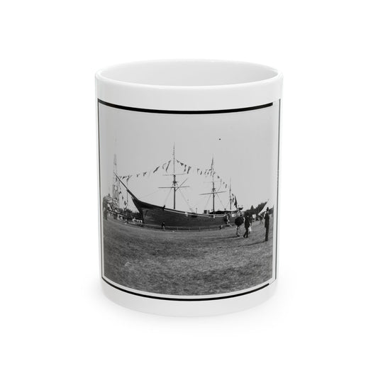 Black and white view of an old sailing ship on a grassy field, decorated with pennant flags and visitors nearby.