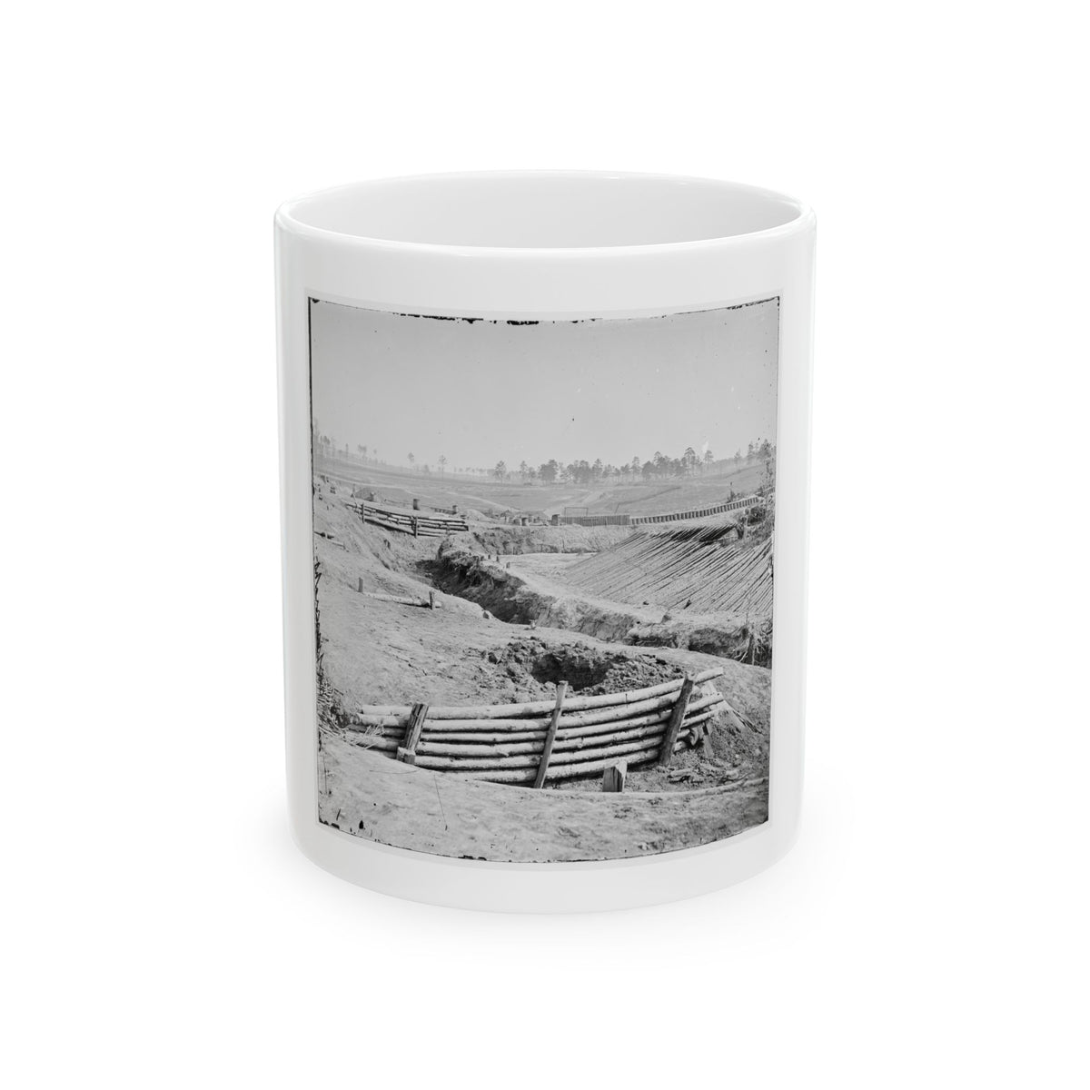 Black and white view of log-faced trenches and sloped earthworks cutting across open ground under a pale sky.