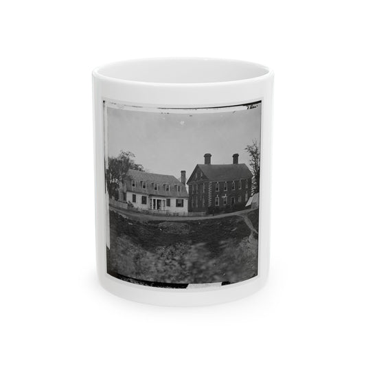 Black-and-white view of a two-storey brick house beside a white farmhouse, with a canvas tent by a dirt road.