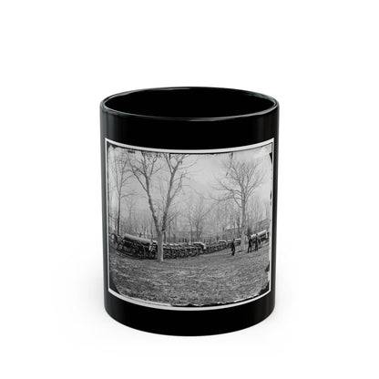 Black and white historical view of covered army wagons lined up on a field beneath bare trees, with two men nearby.