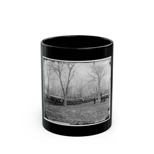 Black and white historical view of covered army wagons lined up on a field beneath bare trees, with two men nearby.