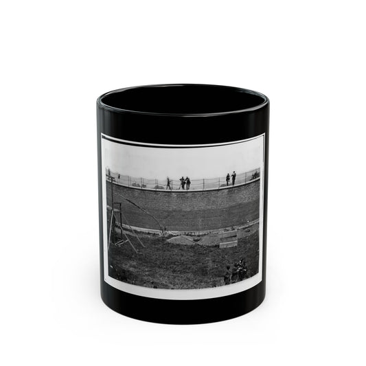 Black and white 1860s view of men on top of a tall brick wall above a grassy field, beside a wooden platform.