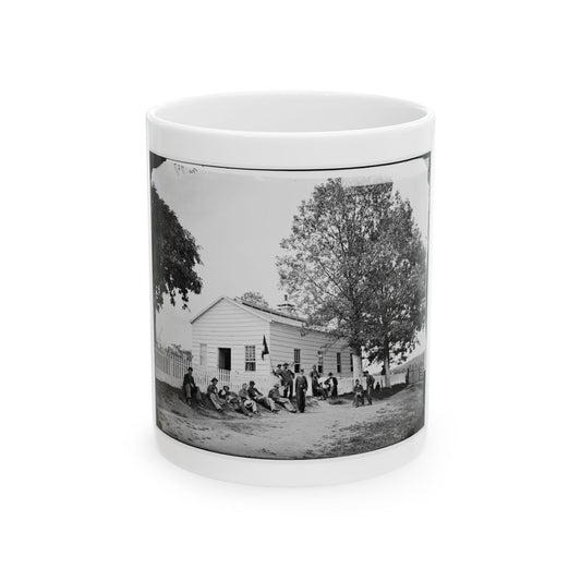 Black and white 19th-century view of men resting outside a white clapboard house beside a picket fence and tree.
