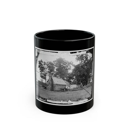 Black and white view of a log cabin with a stone chimney, grazing horses and split-rail fencing.