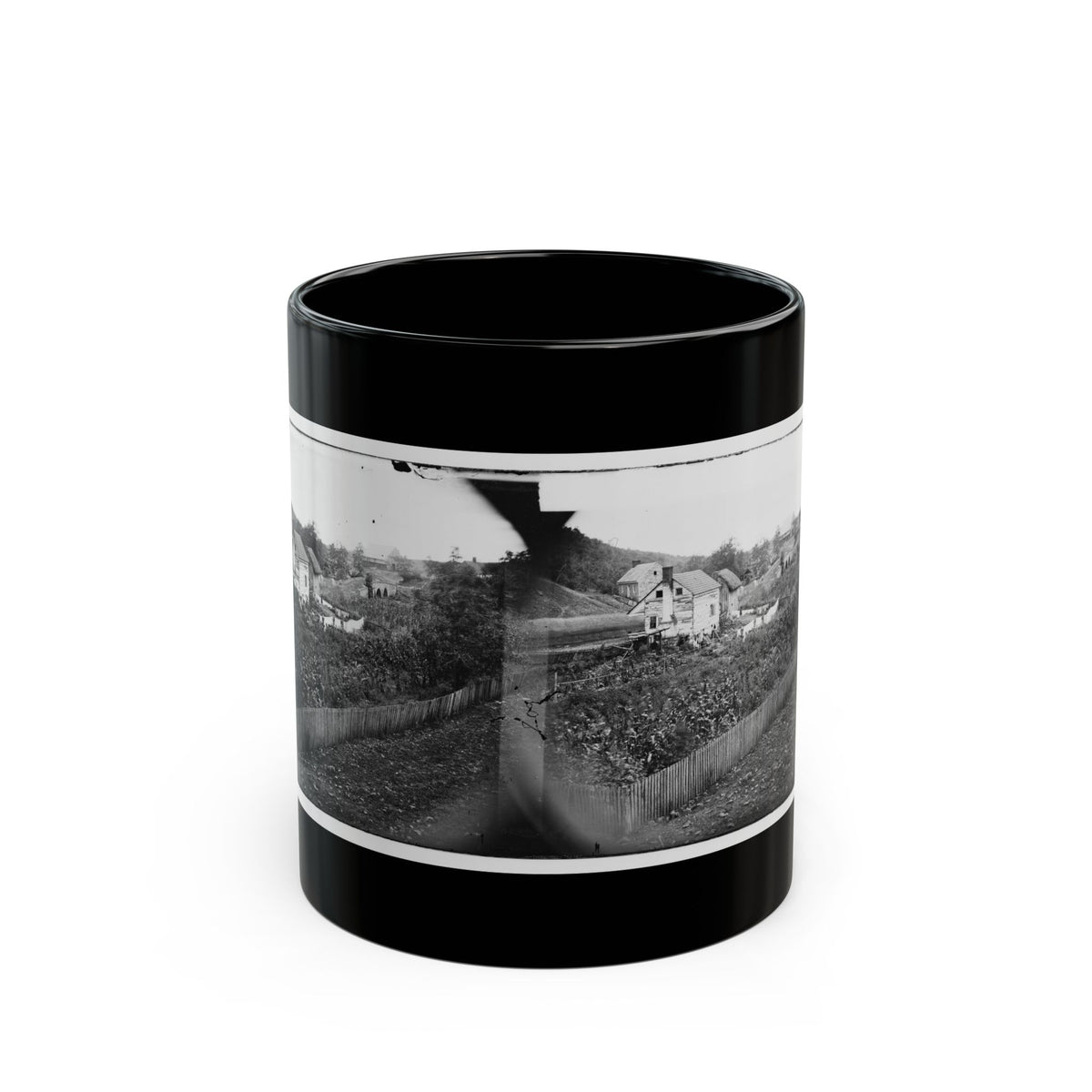 Black-and-white 1860s stereo print of wooden farmhouses, a garden plot and a picket fence on a hillside.