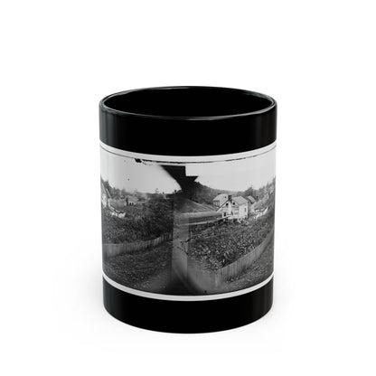 Black-and-white 1860s stereo print of wooden farmhouses, a garden plot and a picket fence on a hillside.