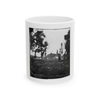 Black and white scene of brick chimneys standing among ruins and trees above a field of wildflowers.