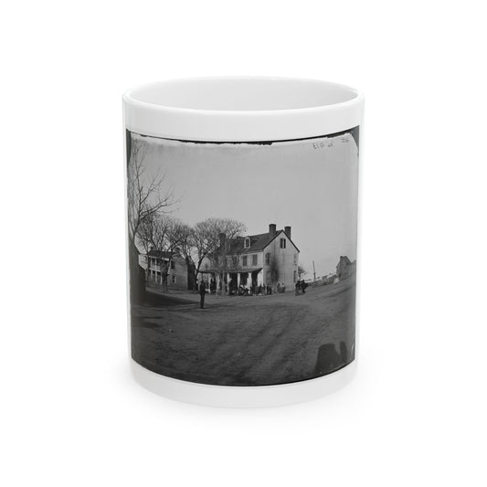 Black and white view of a two-storey historic house with a columned porch and small figures on a dirt street.
