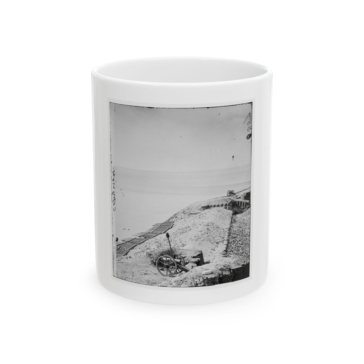 Black-and-white view of a cannon on a sandy fort embankment overlooking open water under a pale sky.