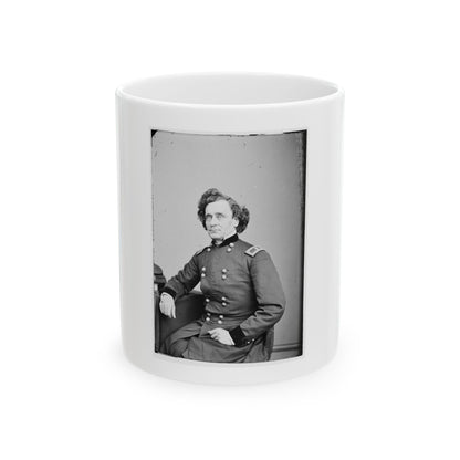 Black and white portrait of a curly-haired man in a dark double-breasted officer's coat, seated beside a table.