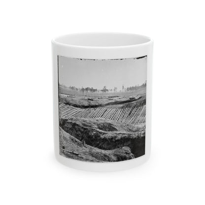 Black and white view of earthworks with rows of sharpened timber stakes angled across embankments under a pale sky.