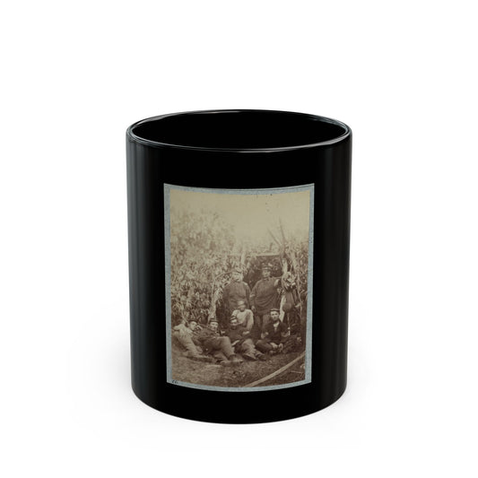 Sepia print showing a group of soldiers in forage caps resting among tall corn stalks in a field.