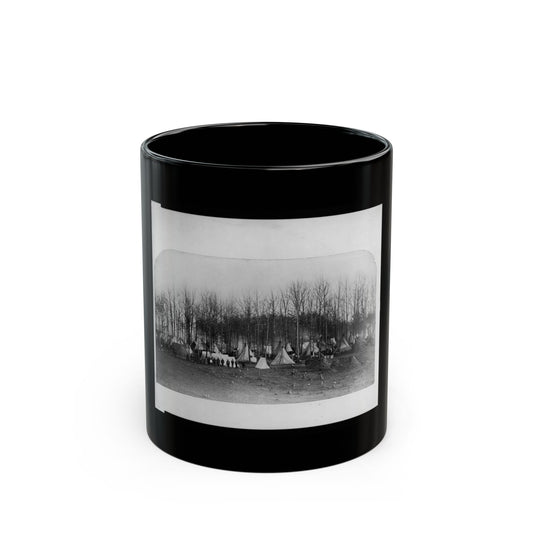 Black and white scene of a camp of conical canvas tents among bare trees, with people standing in front.