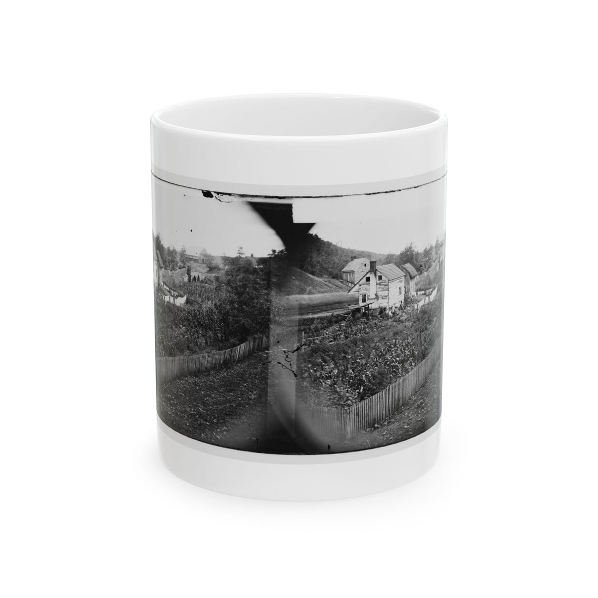 Black-and-white 1860s stereo print of wooden farmhouses, a garden plot and a picket fence on a hillside.