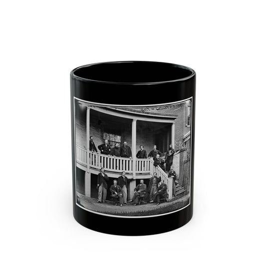 Black and white group view of about fifteen men in period dress on a brick house's veranda and steps.