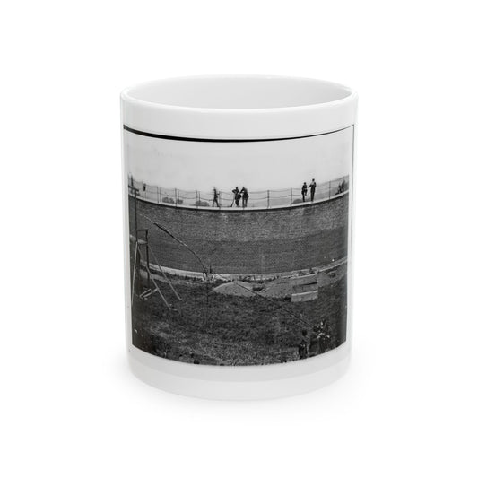 Black and white 1860s view of men on top of a tall brick wall above a grassy field, beside a wooden platform.