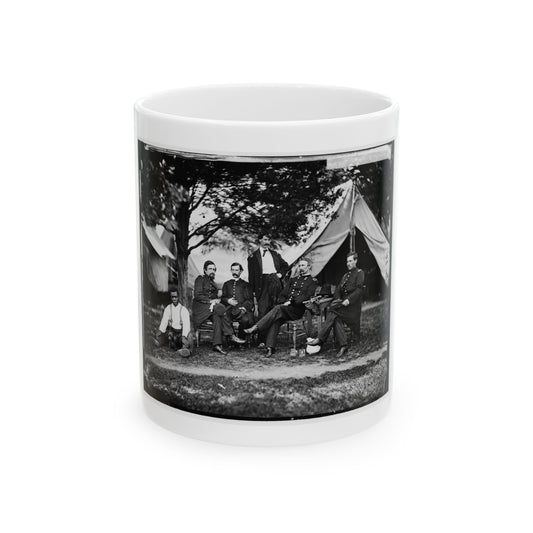Black and white group view of six men before a canvas tent under a tree, one seated with a small dog.