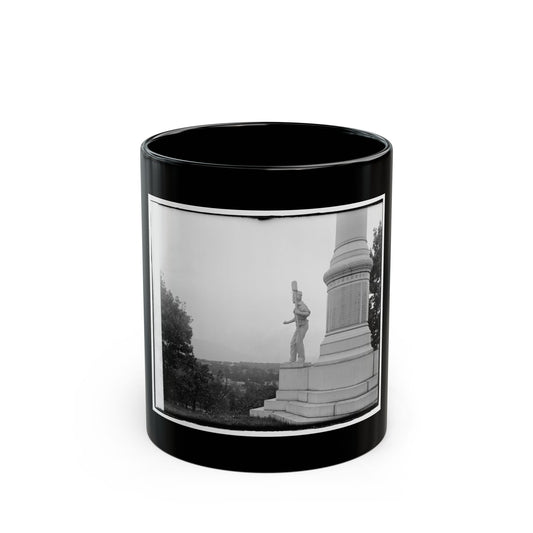 Black and white view of a stone soldier statue holding a rifle beside a tall monument column, valley beyond.