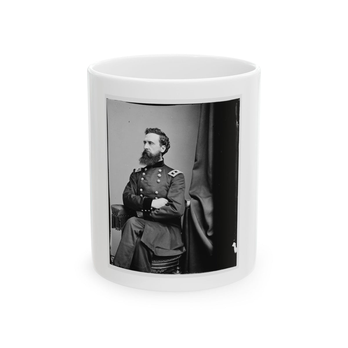 Black and white vintage portrait of a bearded officer seated by a dark drape with arms folded, in uniform.