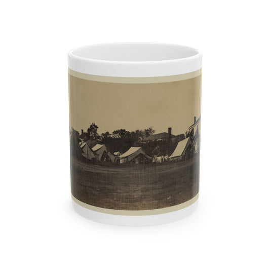 Sepia scene of a row of canvas army tents on an open field, with a two-storey house and trees behind.