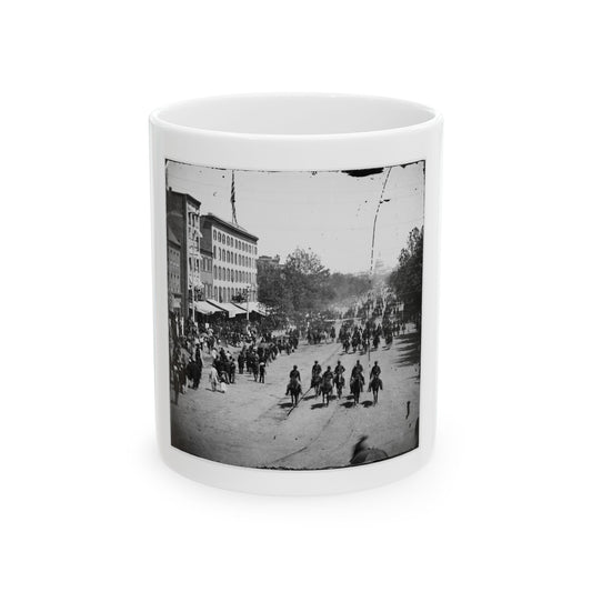 Black and white 1860s view of mounted riders and crowds on a city avenue, with the Capitol dome in the distance.