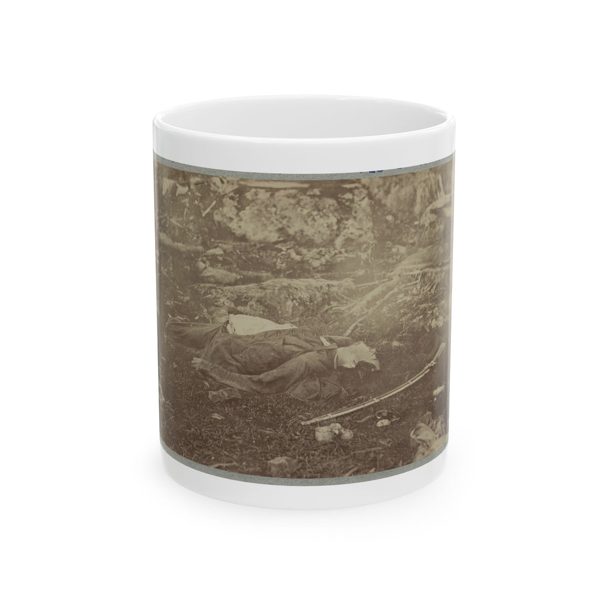 Sepia print of a fallen soldier lying on grass among rocks, with a rifle and a hat on the ground nearby.