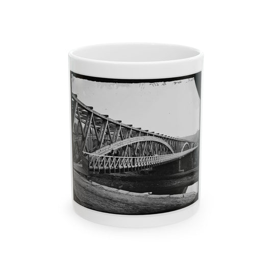 Black and white 1860s view of a long wooden truss bridge over a river, with a few men standing on its deck.