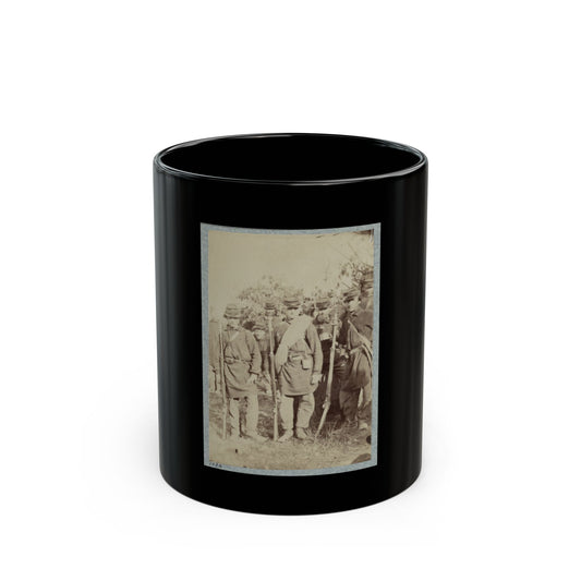 Sepia-toned print of a group of uniformed soldiers standing with rifles in a field before leafy bushes.