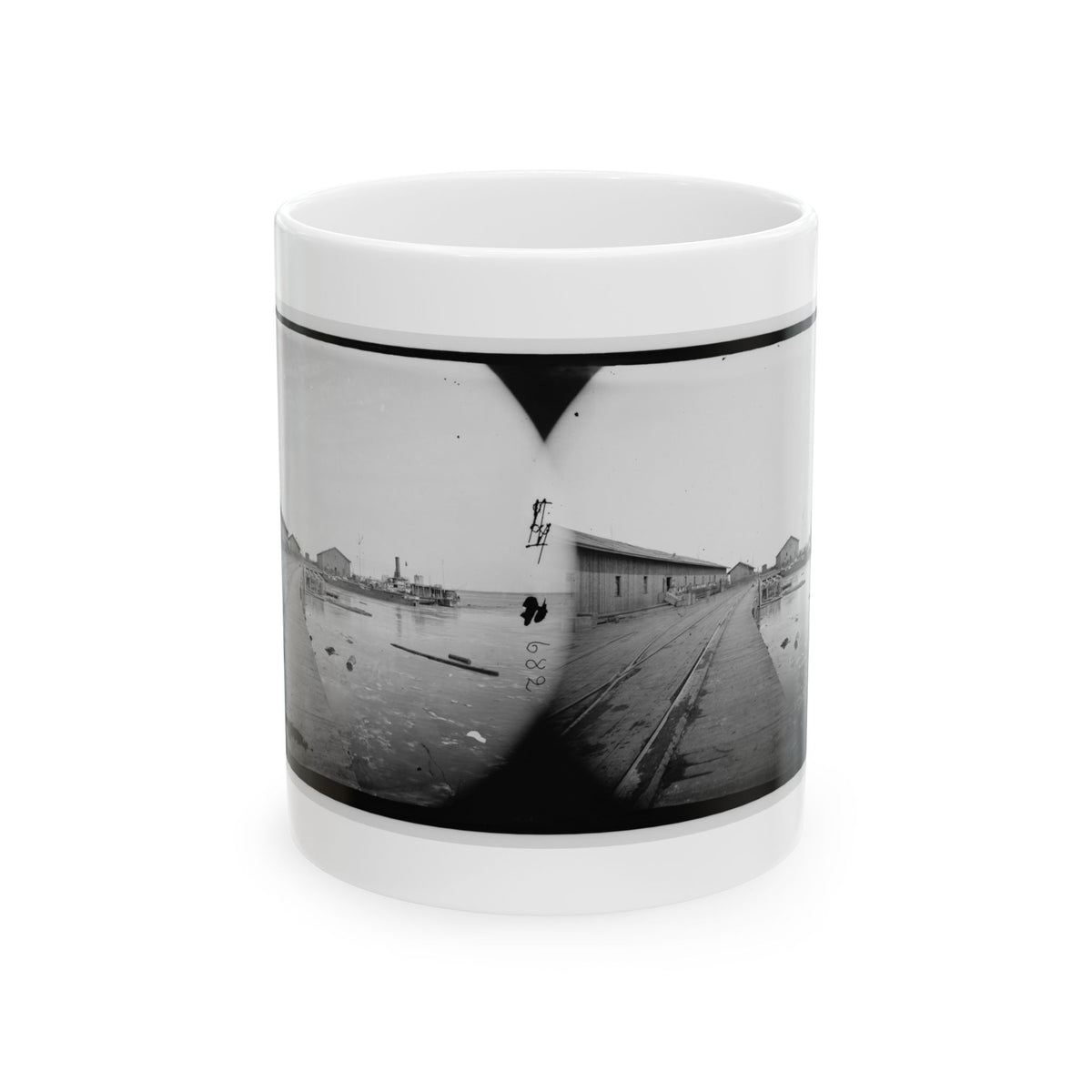 Black and white stereograph of a wooden wharf with rail tracks, warehouses and a steamboat moored on the water.