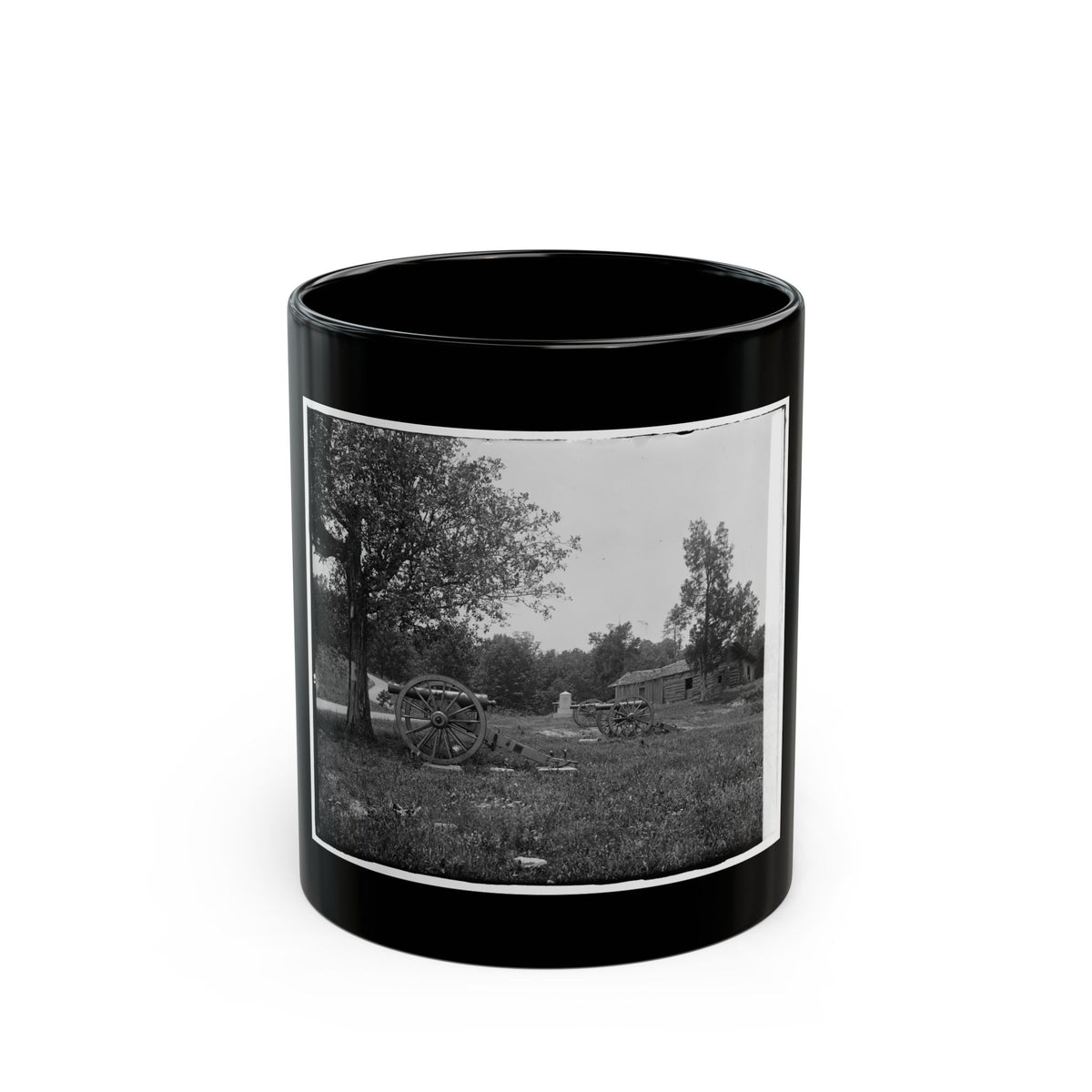 Black and white scene of two cannons on a grassy field beside a log cabin and a large oak tree.