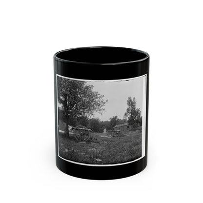 Black and white scene of two cannons on a grassy field beside a log cabin and a large oak tree.