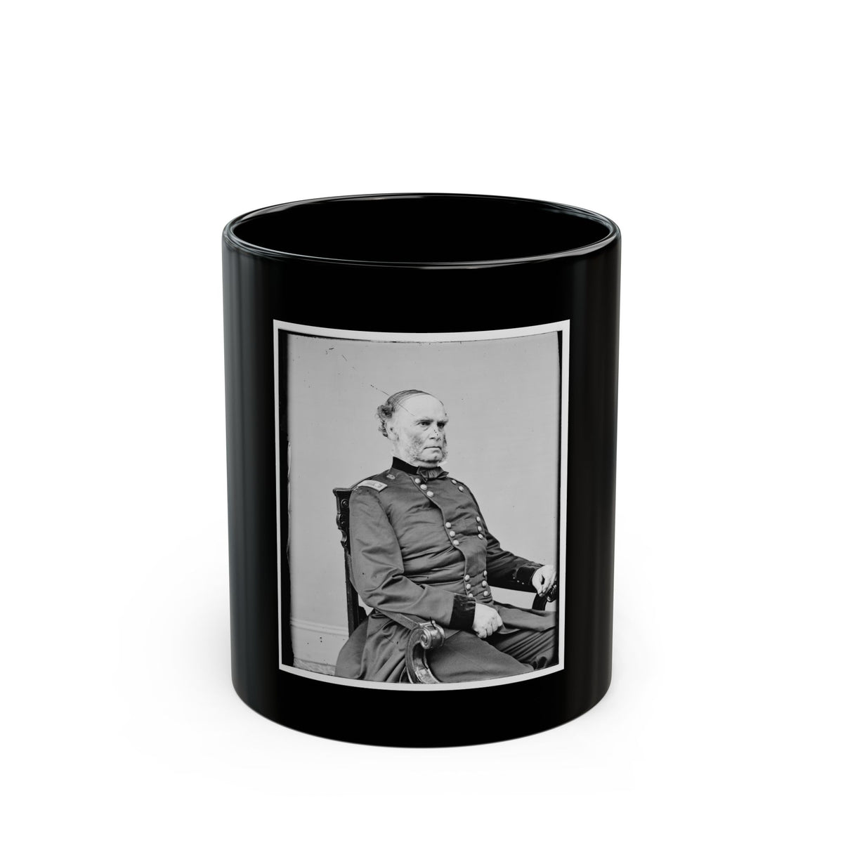 Black and white studio portrait of an older man in a dark button-front coat, seated in a carved wooden chair.