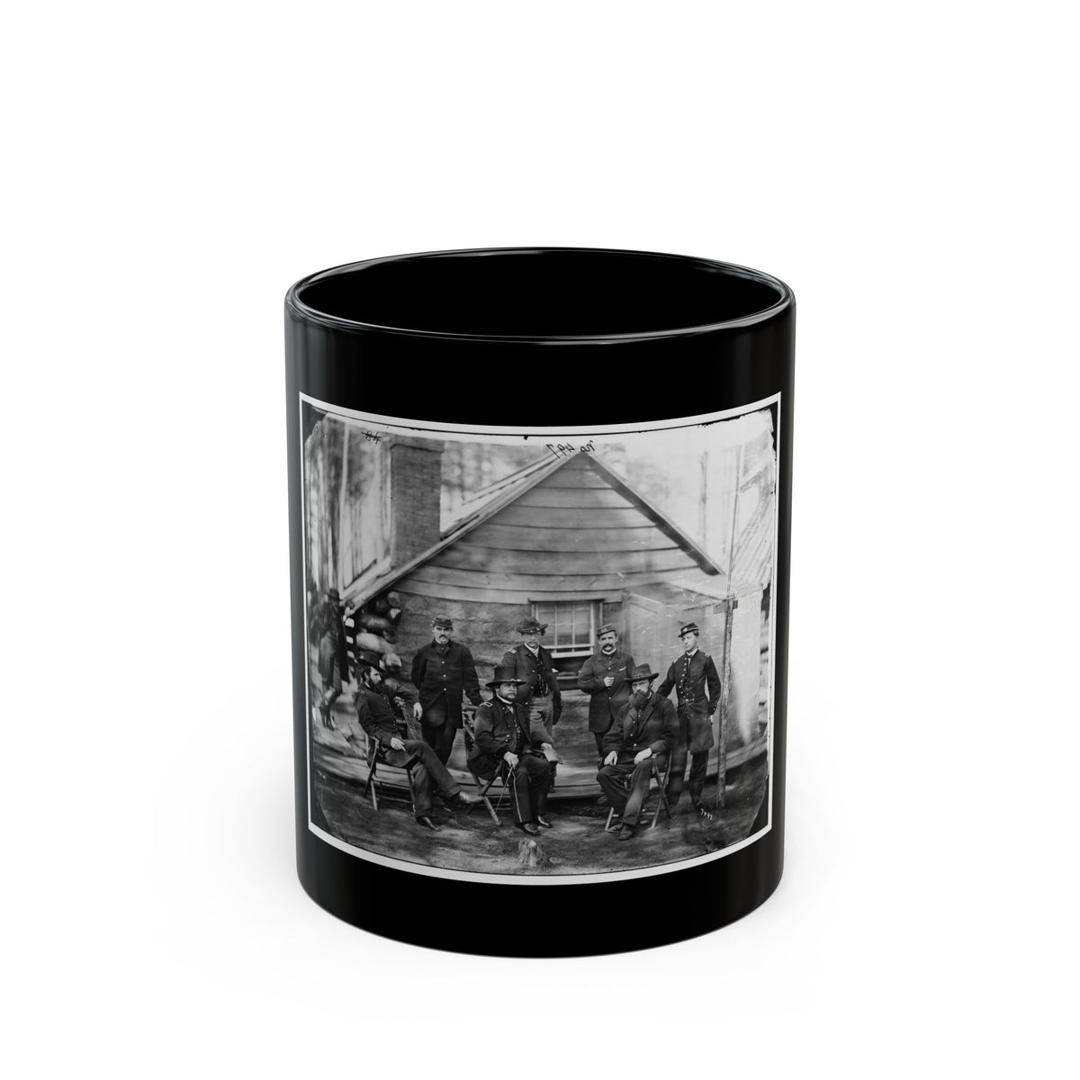 Black-and-white 1860s group view of eight officers in dark uniforms posed outside a log cabin.