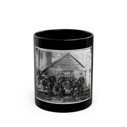 Black-and-white 1860s group view of eight officers in dark uniforms posed outside a log cabin.