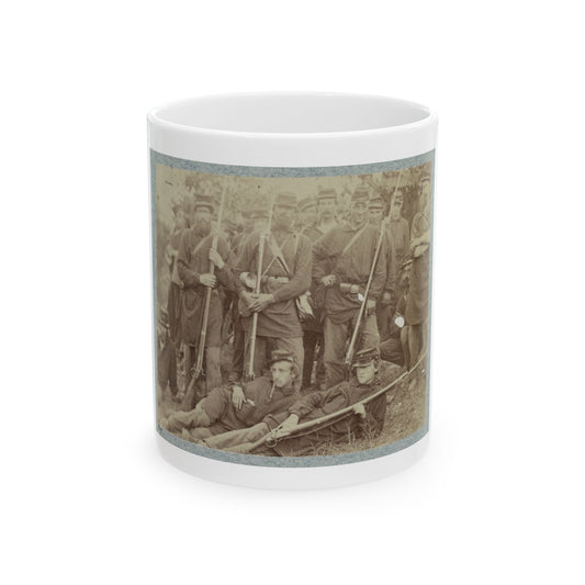 Sepia print showing a crowd of soldiers with rifles, two reclining on the grass in the foreground.