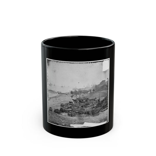 Black and white view of many supply wagons parked on a sandy shore with sailing ships and a pier in the harbor.